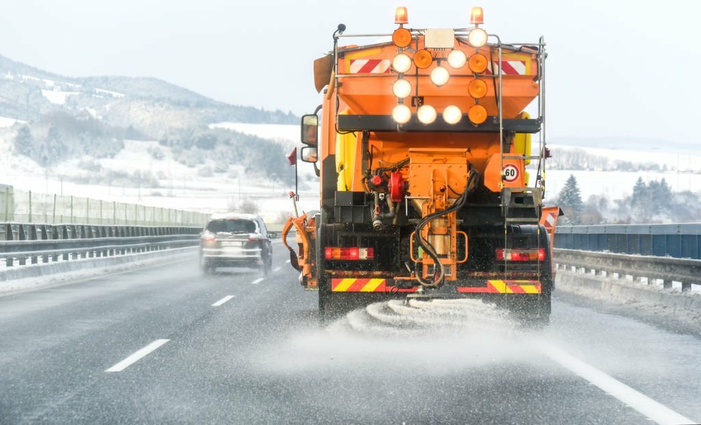 Snow plow on highway salting road. Orange truck deicing street. Maintenance winter vehicle.